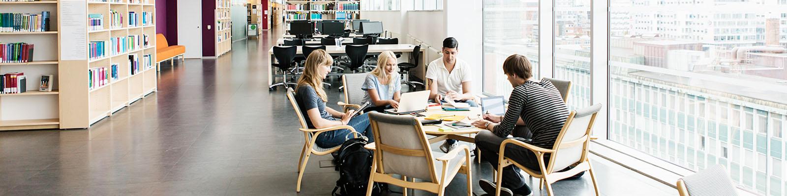 Image of college students with laptops and books working together in a modern library.